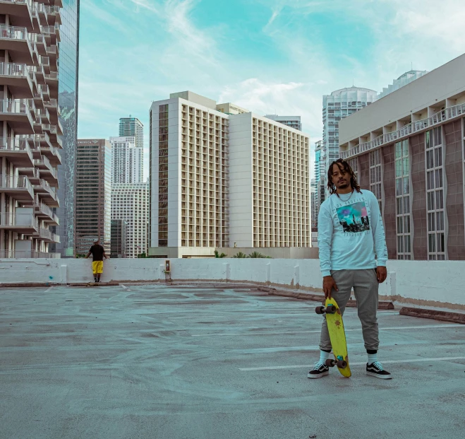 a man is holding a yellow skateboard in front of some tall buildings