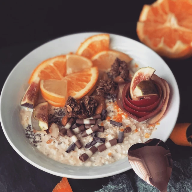 an oatmeal has sliced oranges, chocolate pieces, and a peeled apple