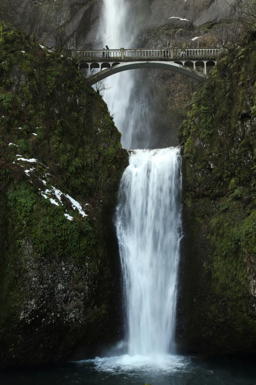 a waterfall is over a small bridge in the middle of the water