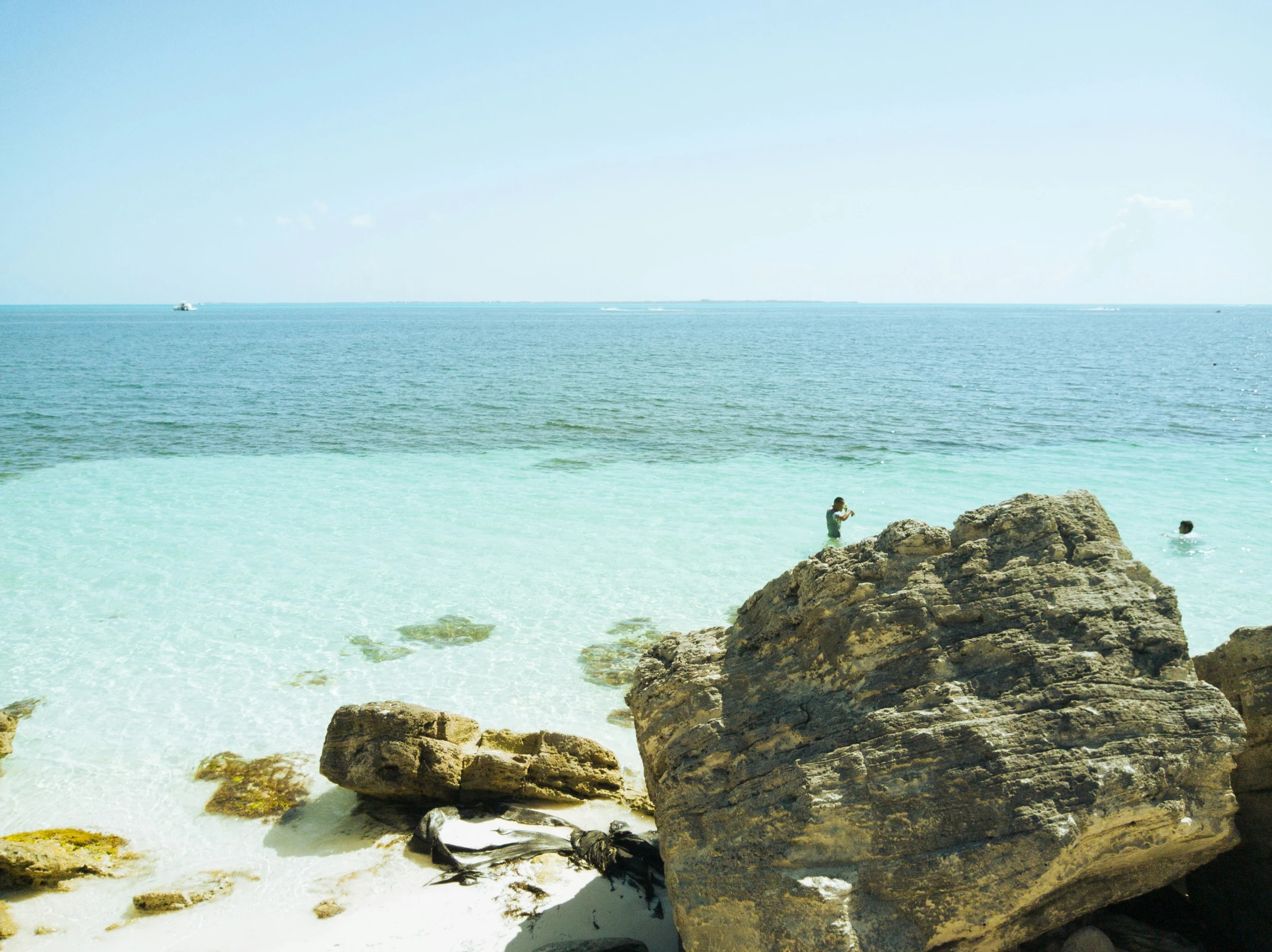 a view of a man standing on the edge of a rock next to the ocean