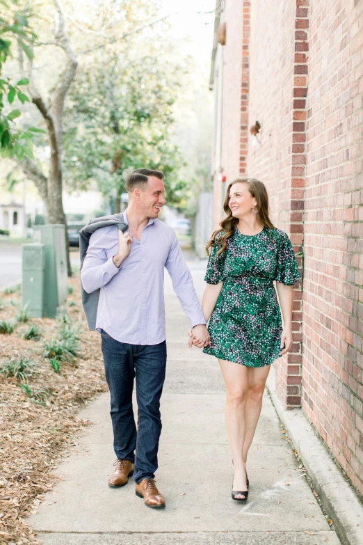 the couple holds hands as they walk on the sidewalk near a brick building