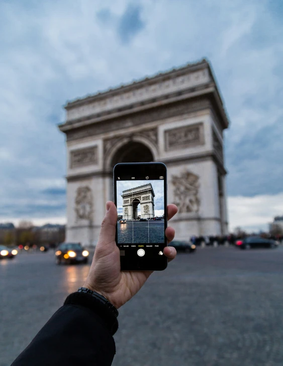 someone holding up a cell phone in front of the arc de trioe triumph