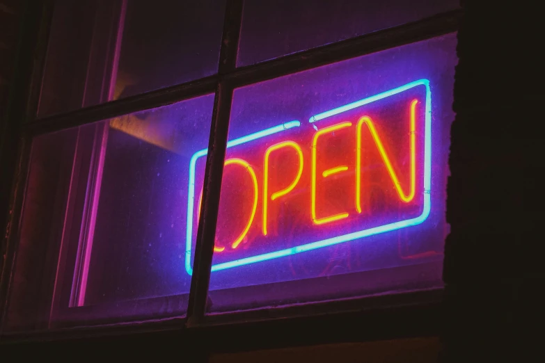 a neon open sign that is lit up in front of a window
