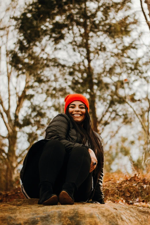 a woman with an orange beanie is sitting in the woods