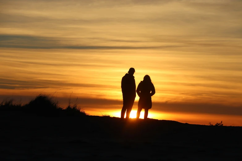 a silhouette of two people standing on top of a hill