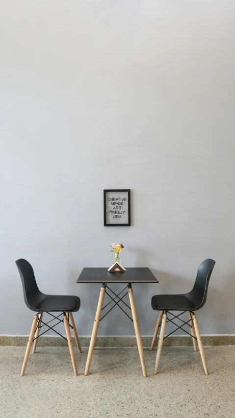 two black eameside chairs and a table against a wall