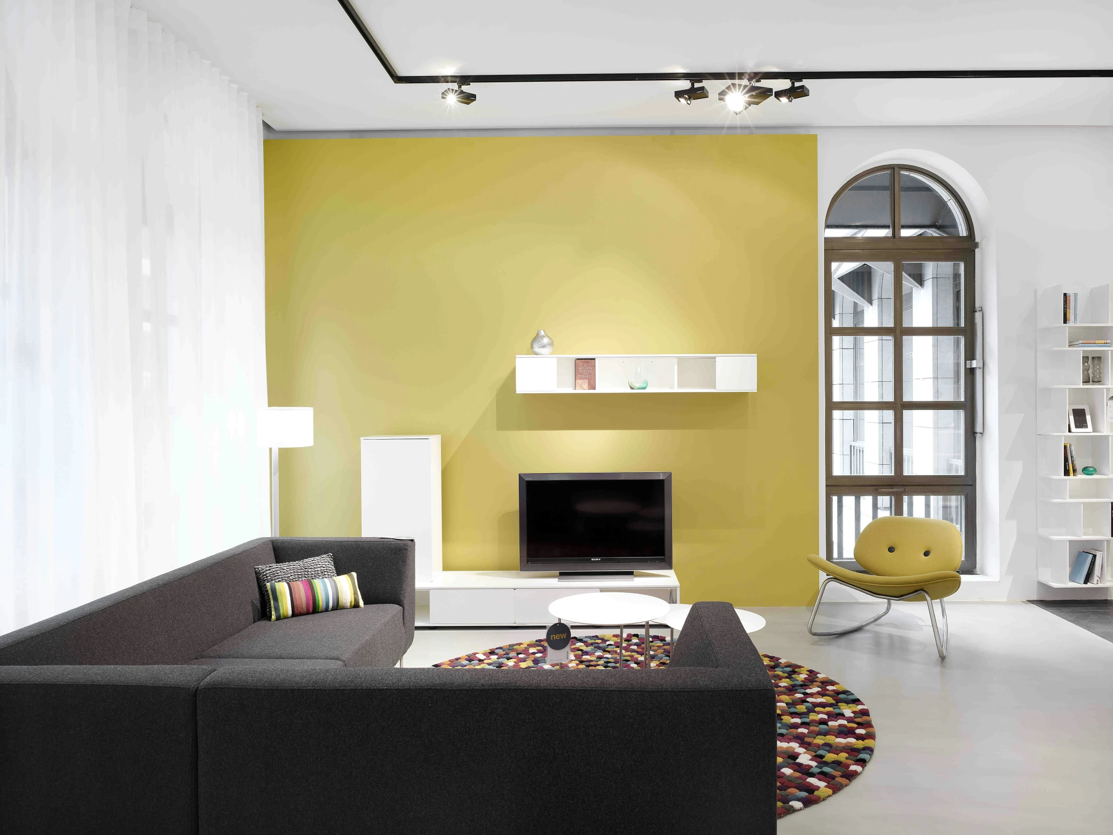 a white and yellow living room has an upholstered couch, table, and bookshelf