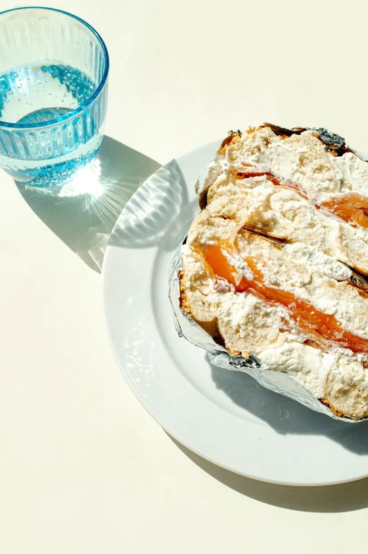 a piece of cake on a white plate next to a blue glass