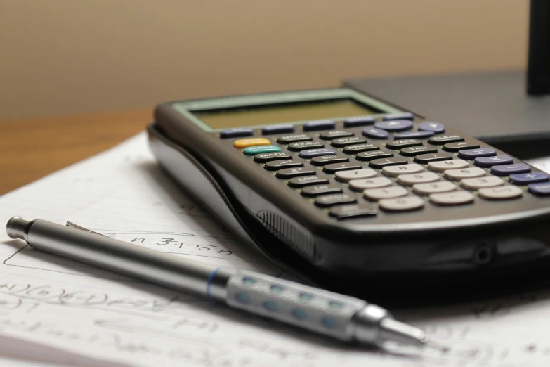 a calculator, pen and computer screen on top of a workbook