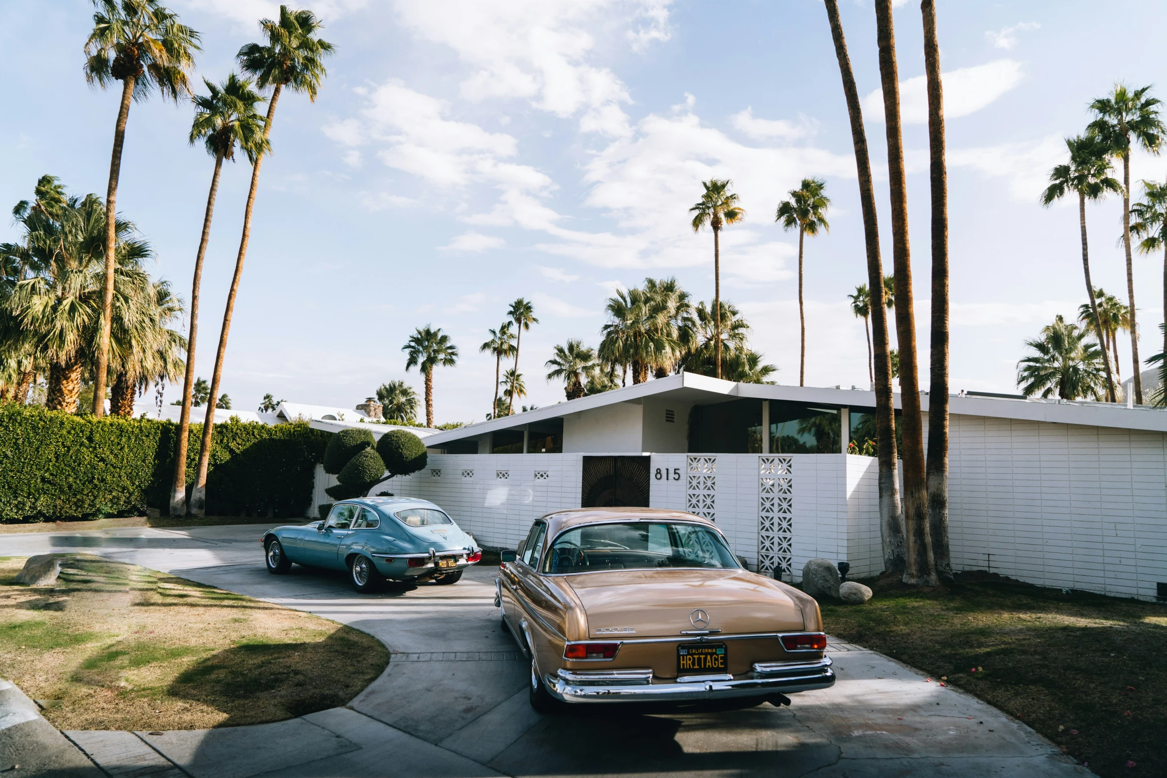 two older cars parked outside a home with palm trees around it