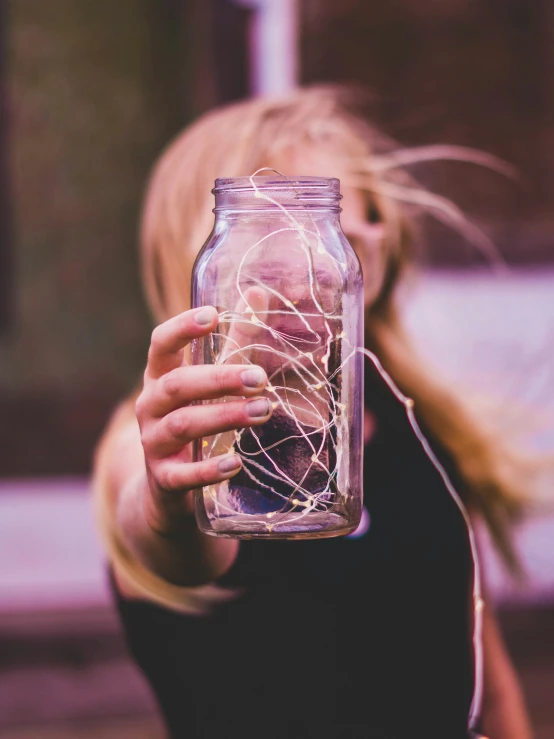 a woman holding a jar with strings inside it