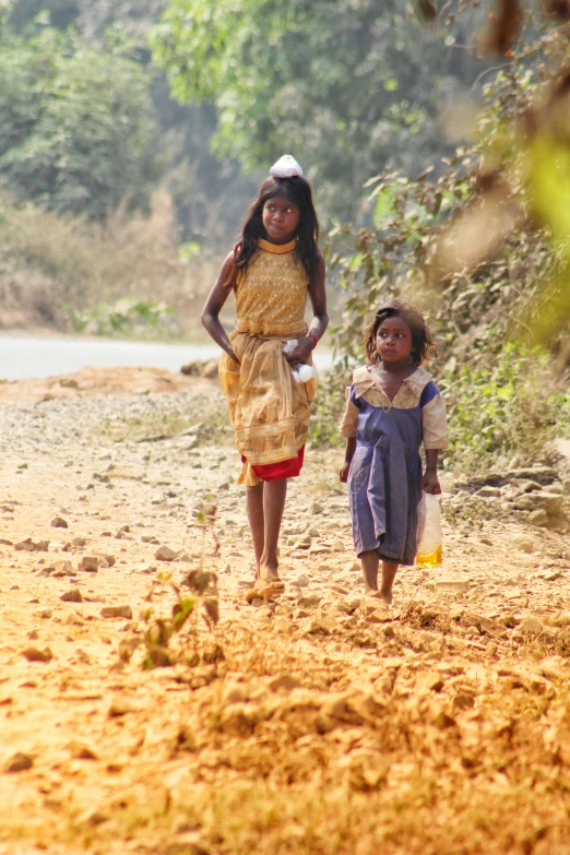 two girls in traditional costumes are walking down a dirt road