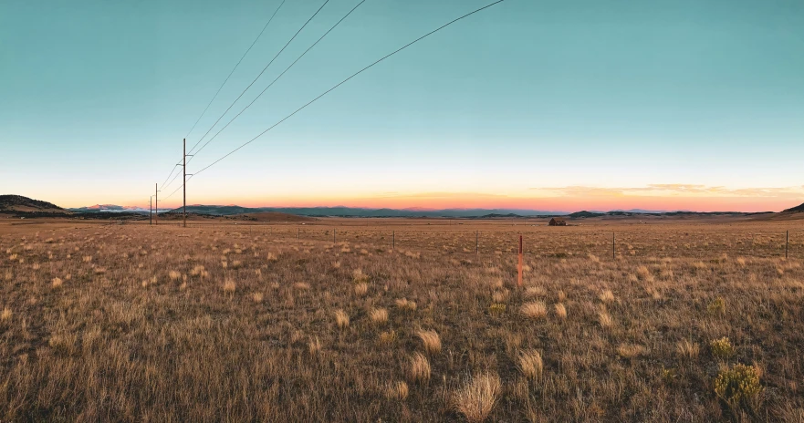 a field with wires, poles and mountains in the background