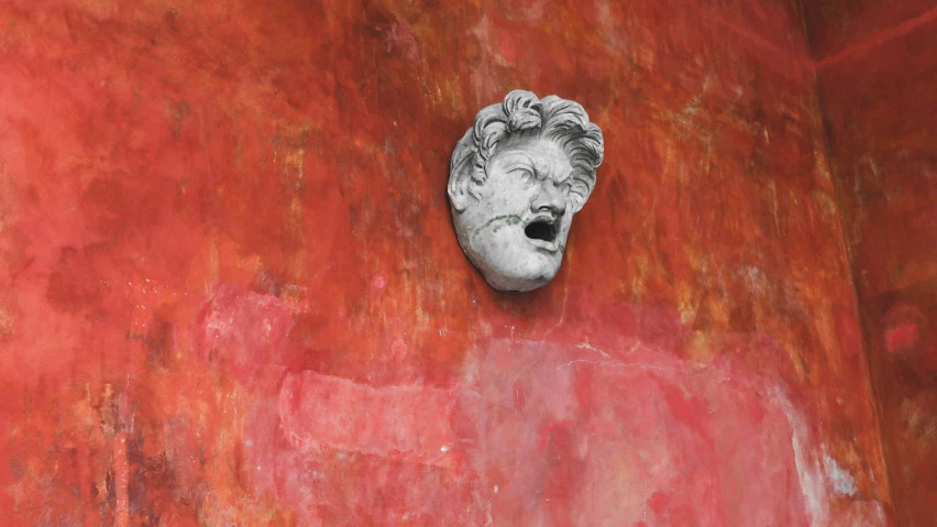 the face of a stone sculpture is against a red wall