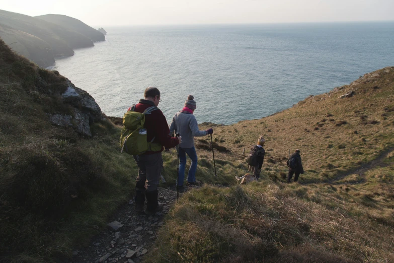 group of hikers standing at the top of a steep cliff looking over the ocean