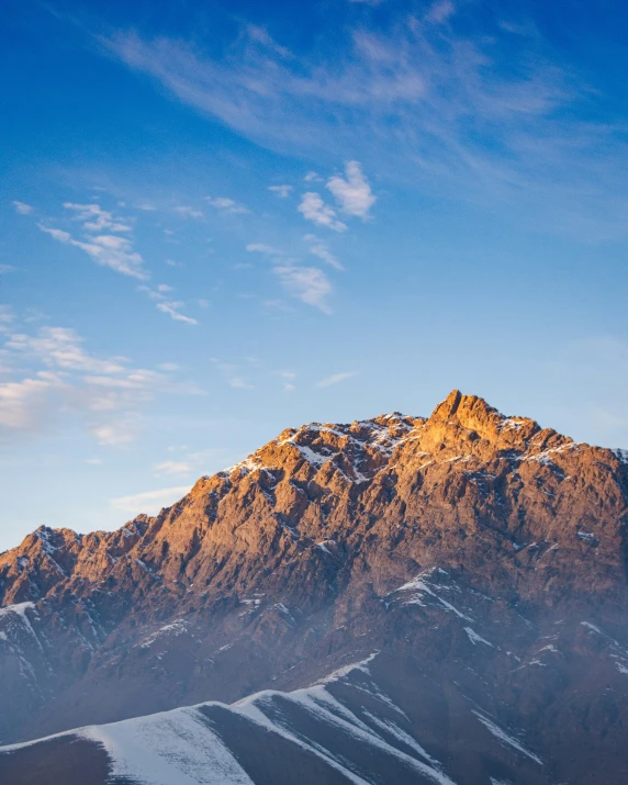 snowy mountains rise against a blue sky and cloud filled sky