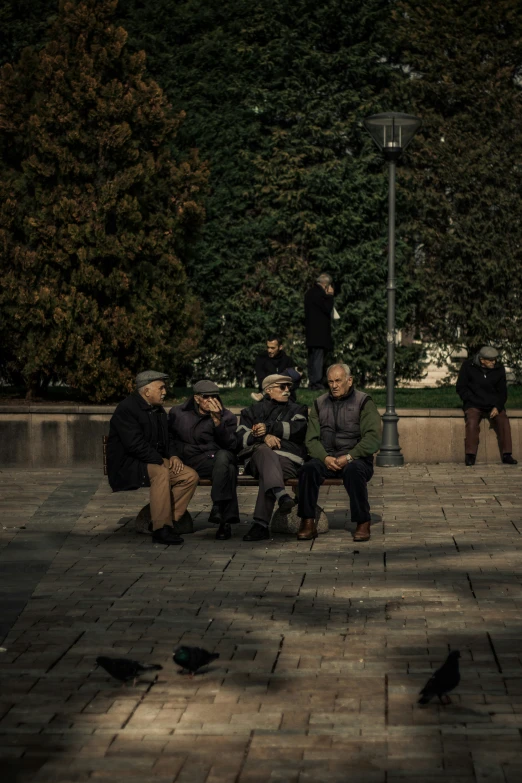 a group of people sitting and standing on a park bench