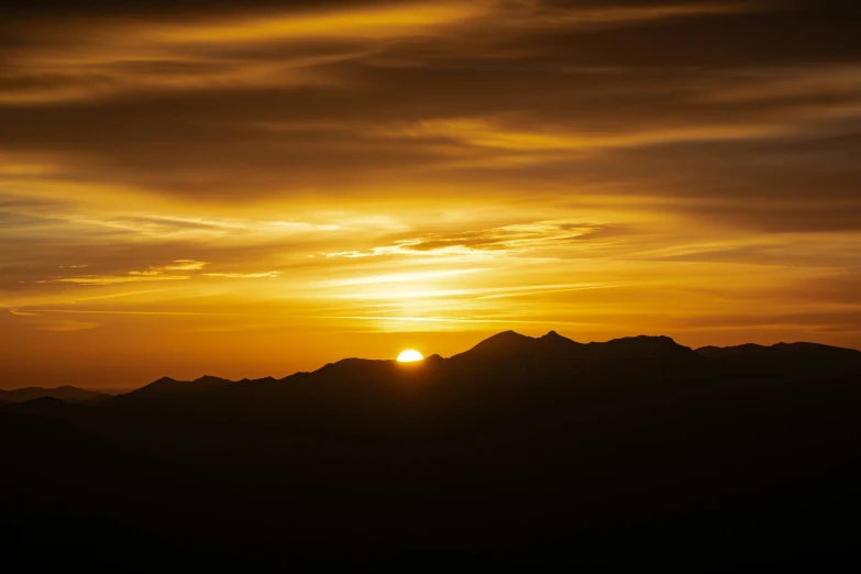 an airplane flying over mountains with the sun setting in the background