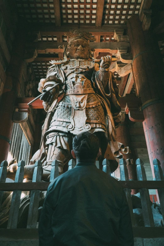 a man looks up at a large wooden statue