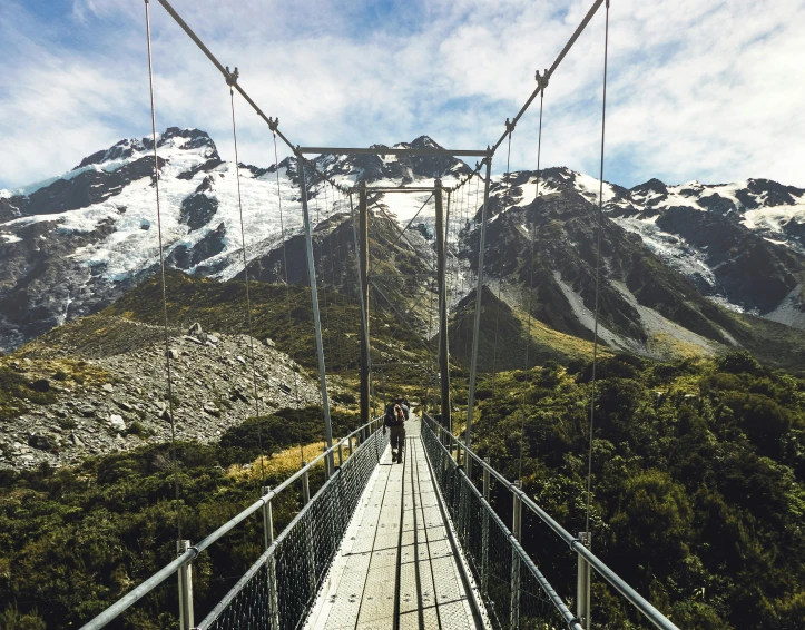 a suspension bridge with a bunch of people on it near some snow covered mountains