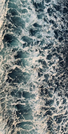 top down view of ocean with small waves and white and blue rocks