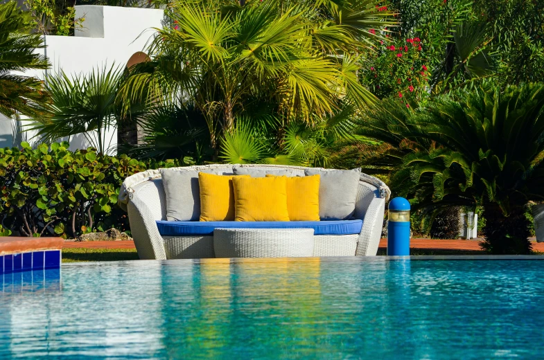 a couch sitting under a tree next to a blue swimming pool