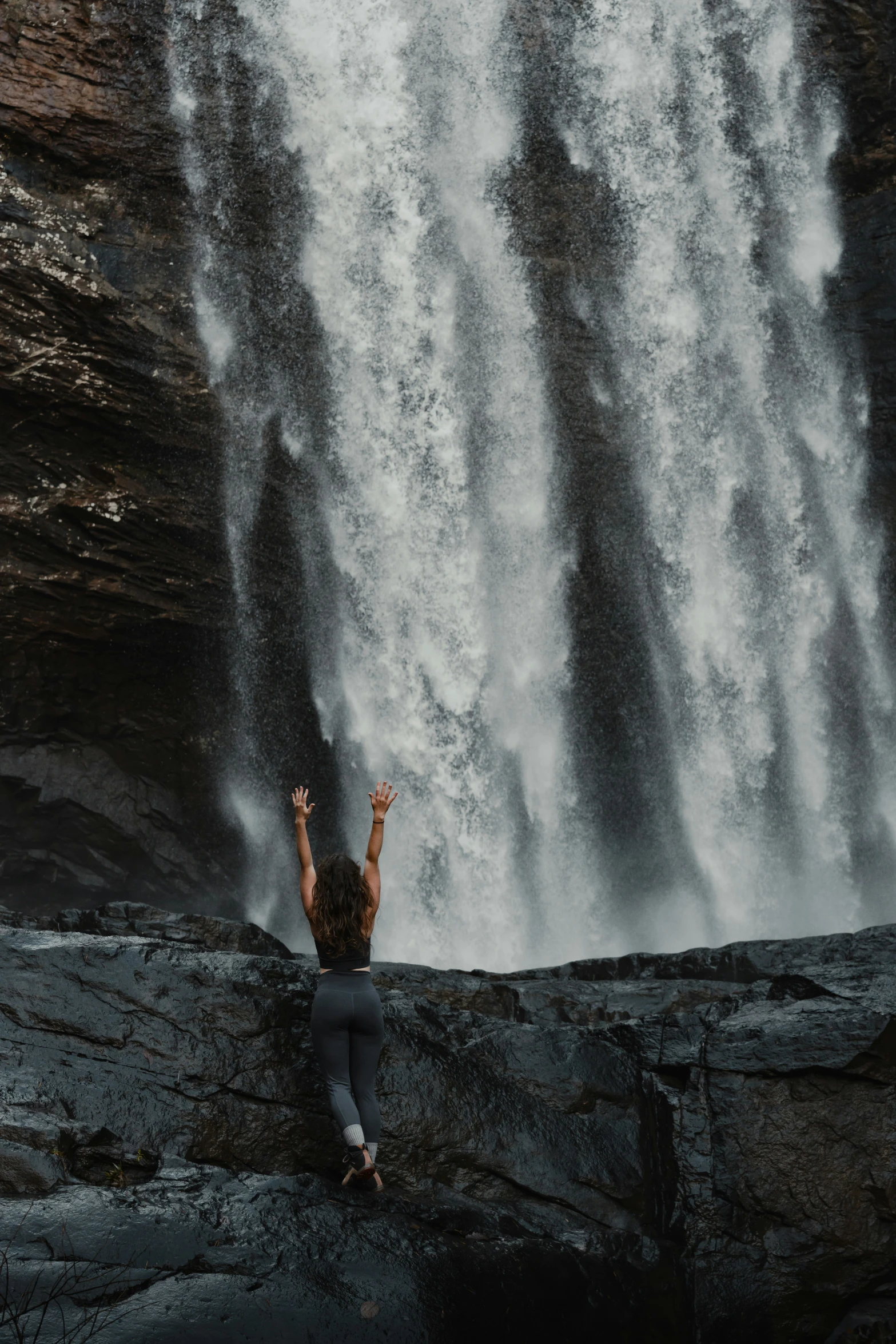 a person standing at the edge of a waterfall pointing up