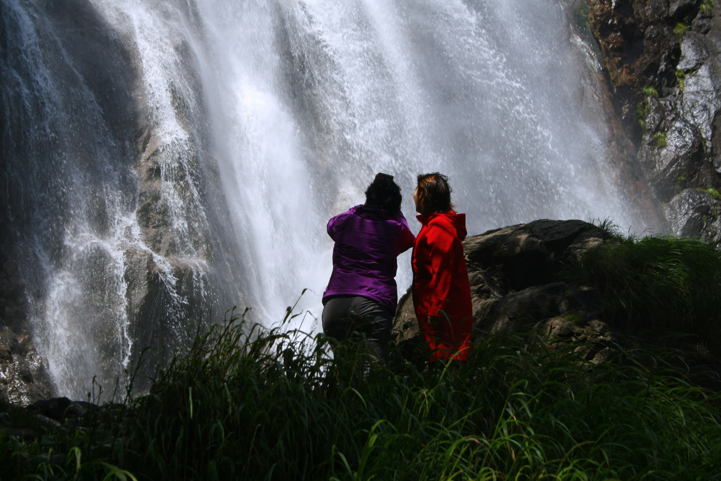 two women in red and purple outfits by a waterfall