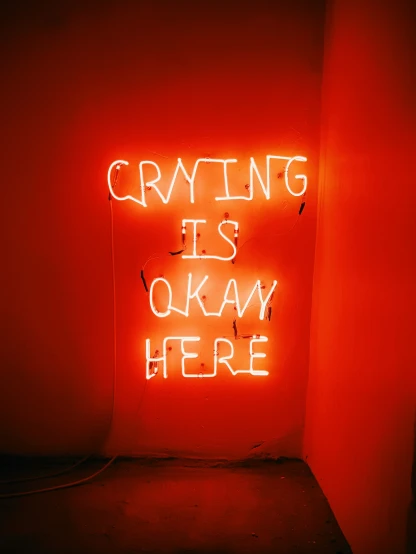 a neon sign that reads crying is okay here