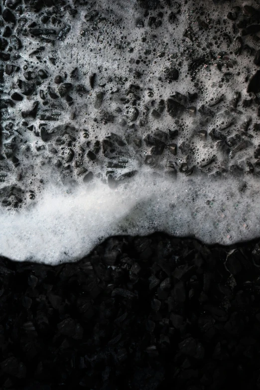 a wave crashing into the black rocks under a cloudy sky