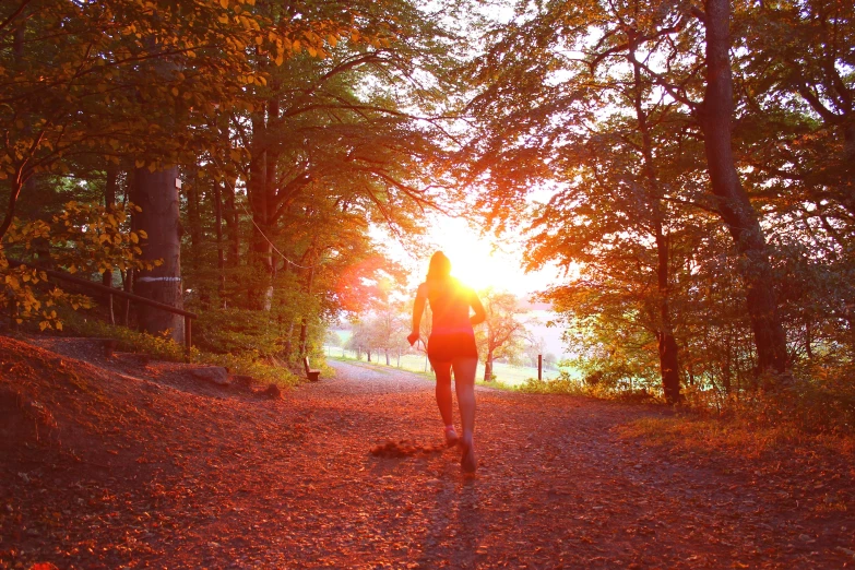 woman walking away from a wooded area into the sunset