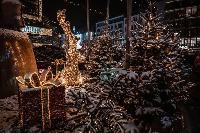 a tree with a gift on top of it, surrounded by lights and snow