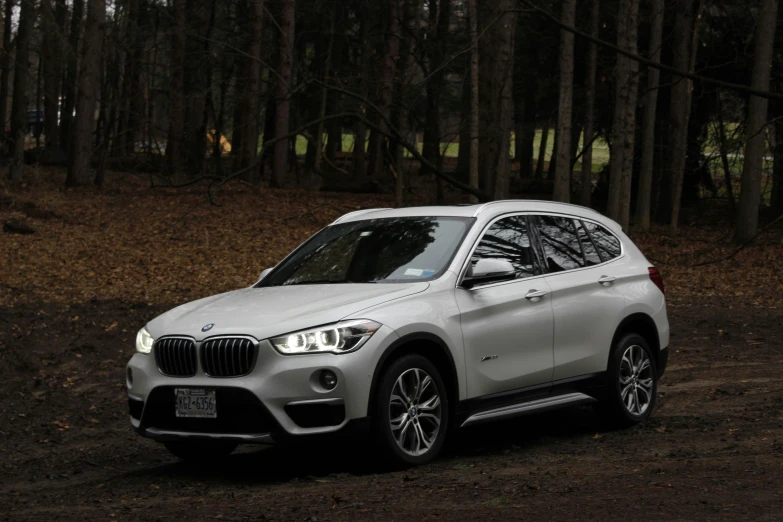 a white bmw suv parked in the middle of the woods