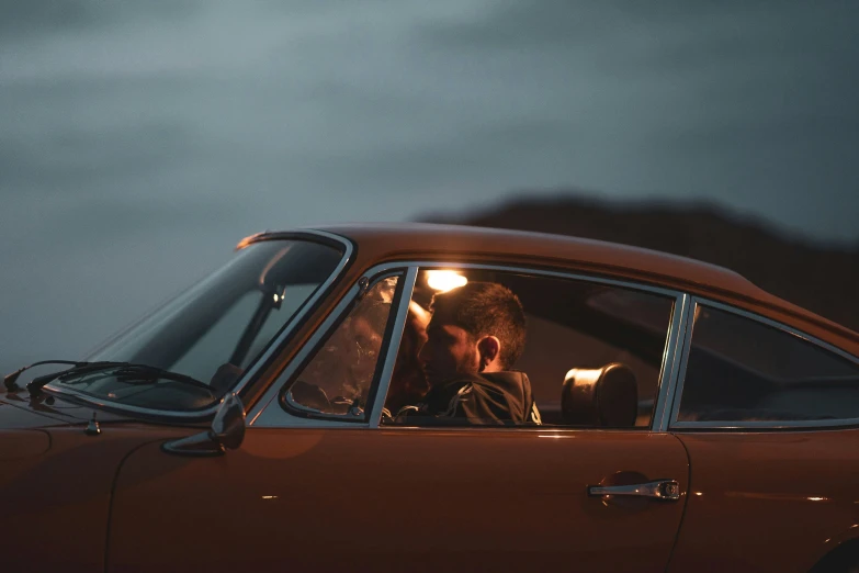 man and woman kissing behind the wheel of a classic car