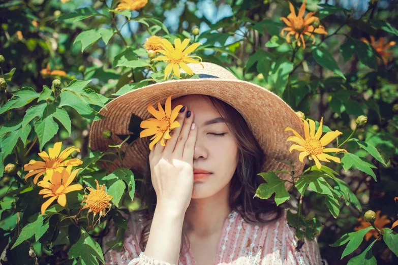 the young woman is wearing a hat and standing in front of a bush