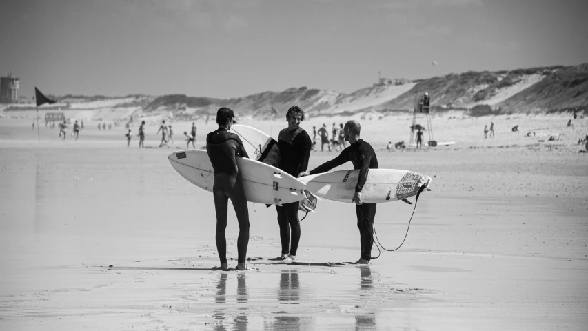 three men with surf boards stand on the beach