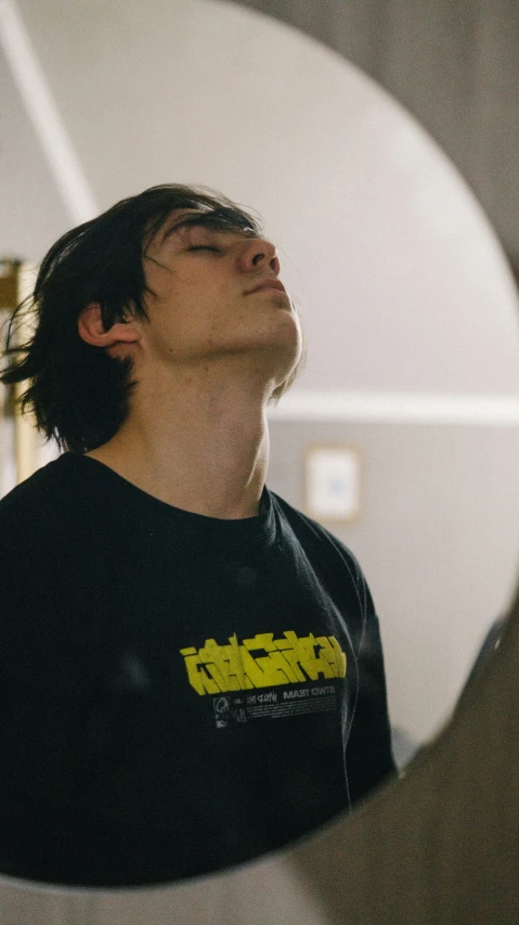 a young man with long hair and a black shirt looks up into the sky