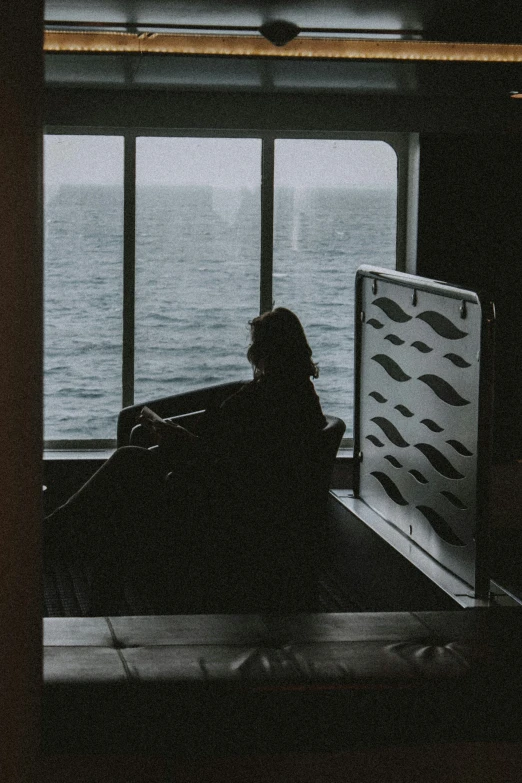 the silhouette of a person sits next to a large window