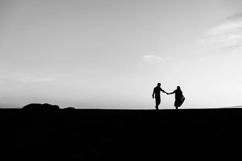 black and white image of a couple walking across the beach