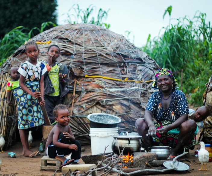 the women and children are preparing food in front of a hut