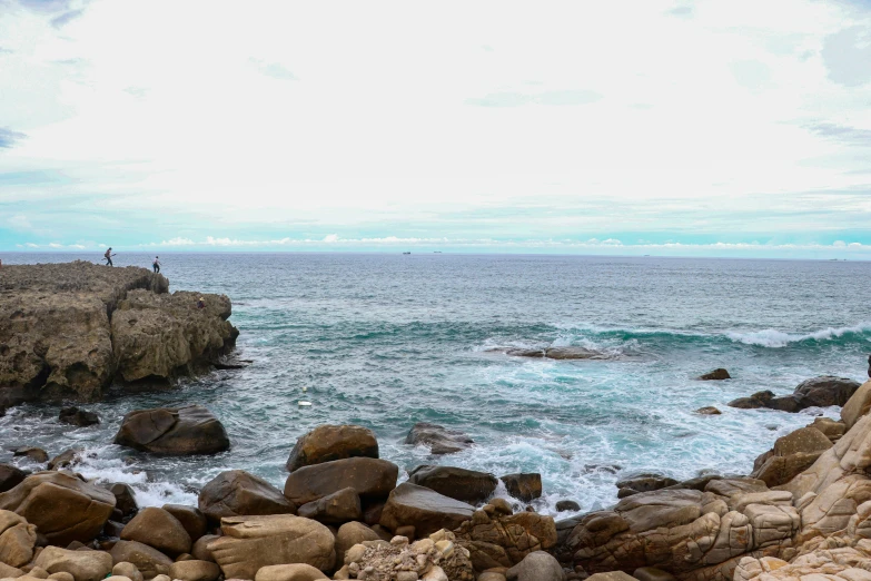 two people standing on rocks near the ocean