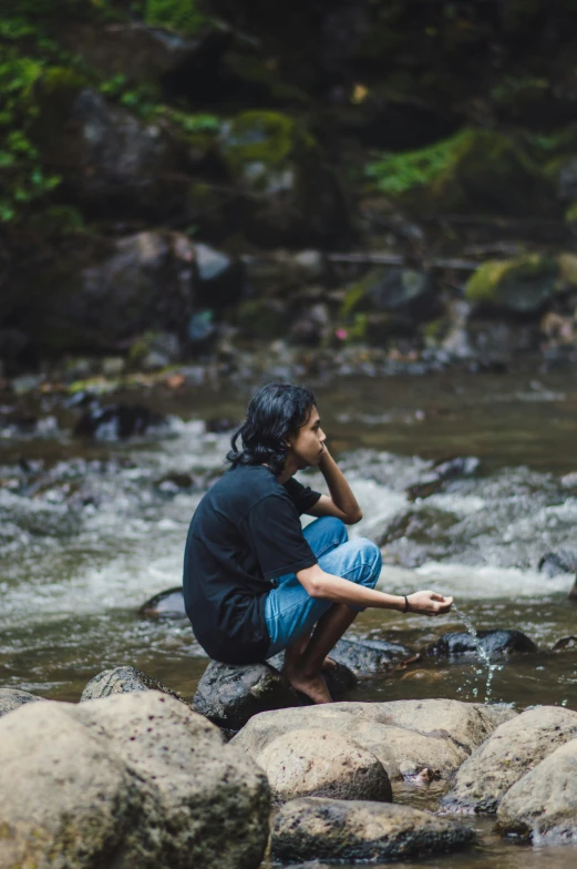 a person sitting on a rock in a stream while looking at soing