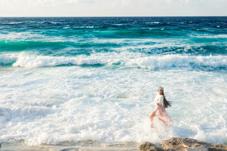 a woman in a long white dress wading in the ocean