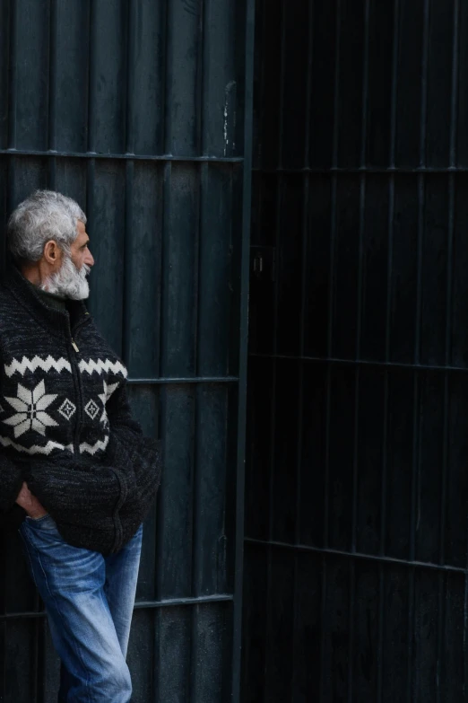 an old man wearing a black sweater and jeans leaning against a metal fence