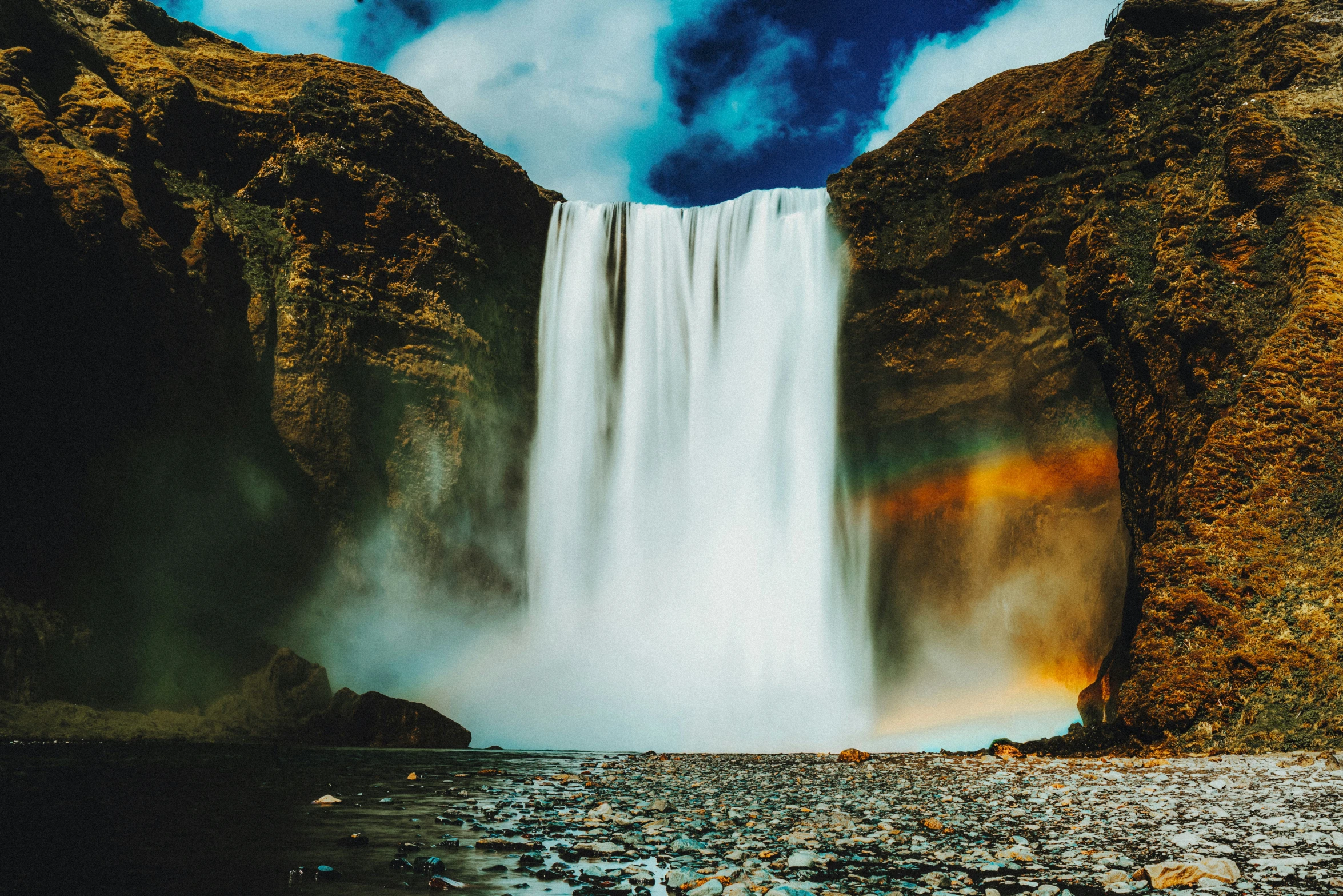 a waterfall with rainbow colored water and sky