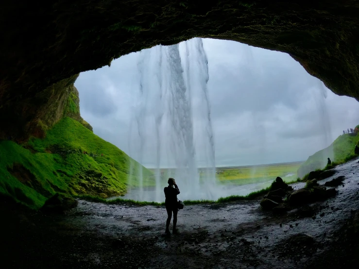 person standing under waterfall while looking at water