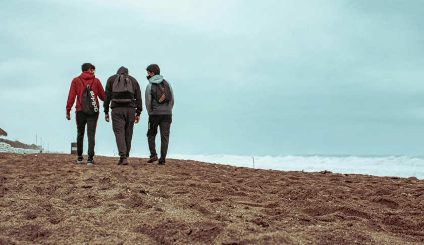 three men walking together on a beach toward the ocean