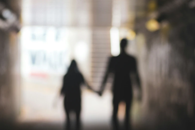 the silhouettes of two people walking in an indoor tunnel