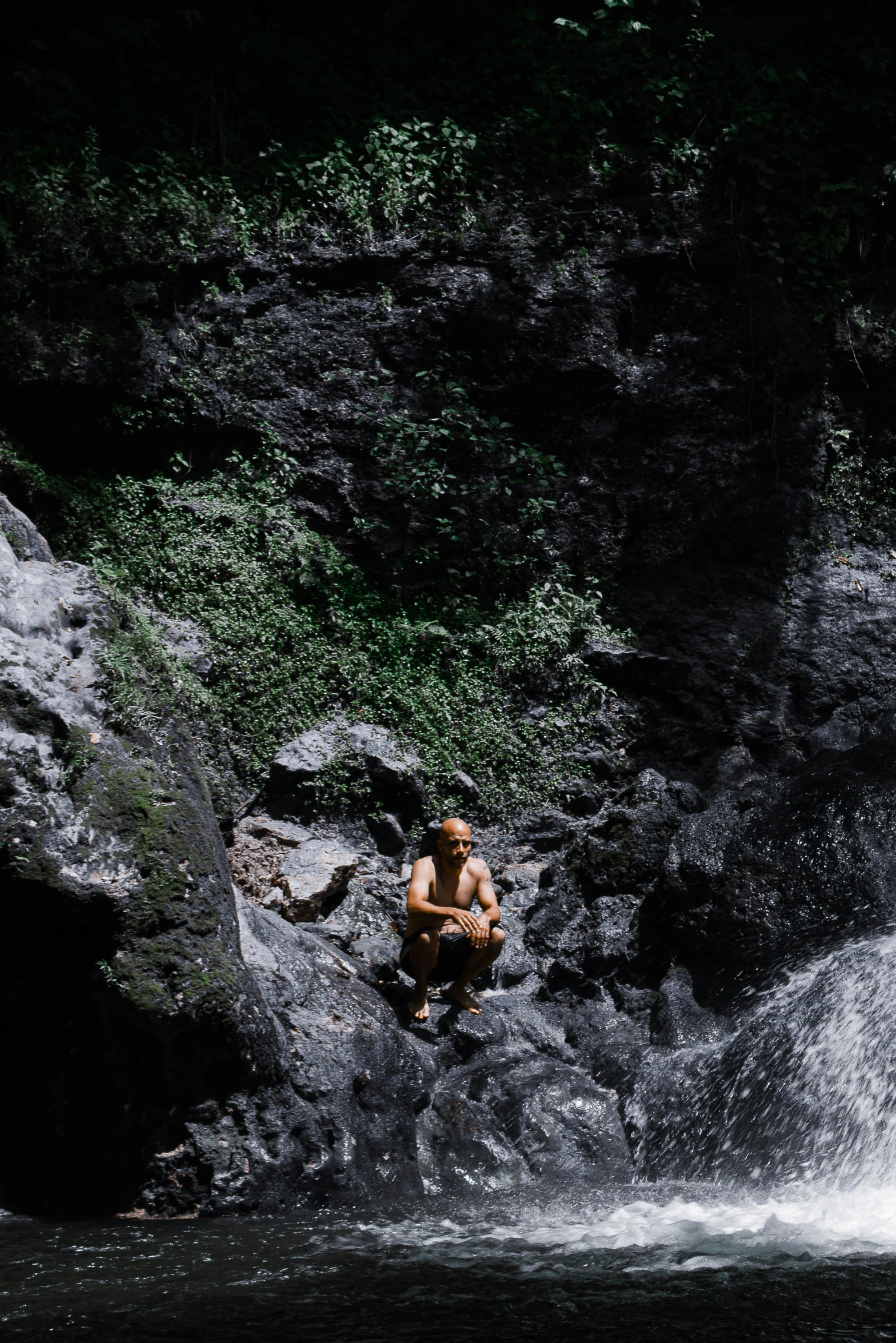 a man wading on rocks in front of a waterfall