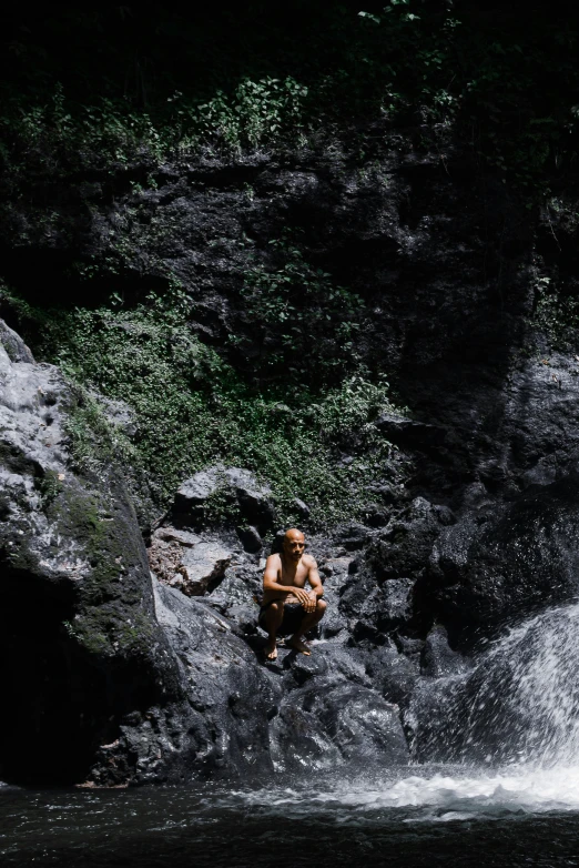 a man wading on rocks in front of a waterfall